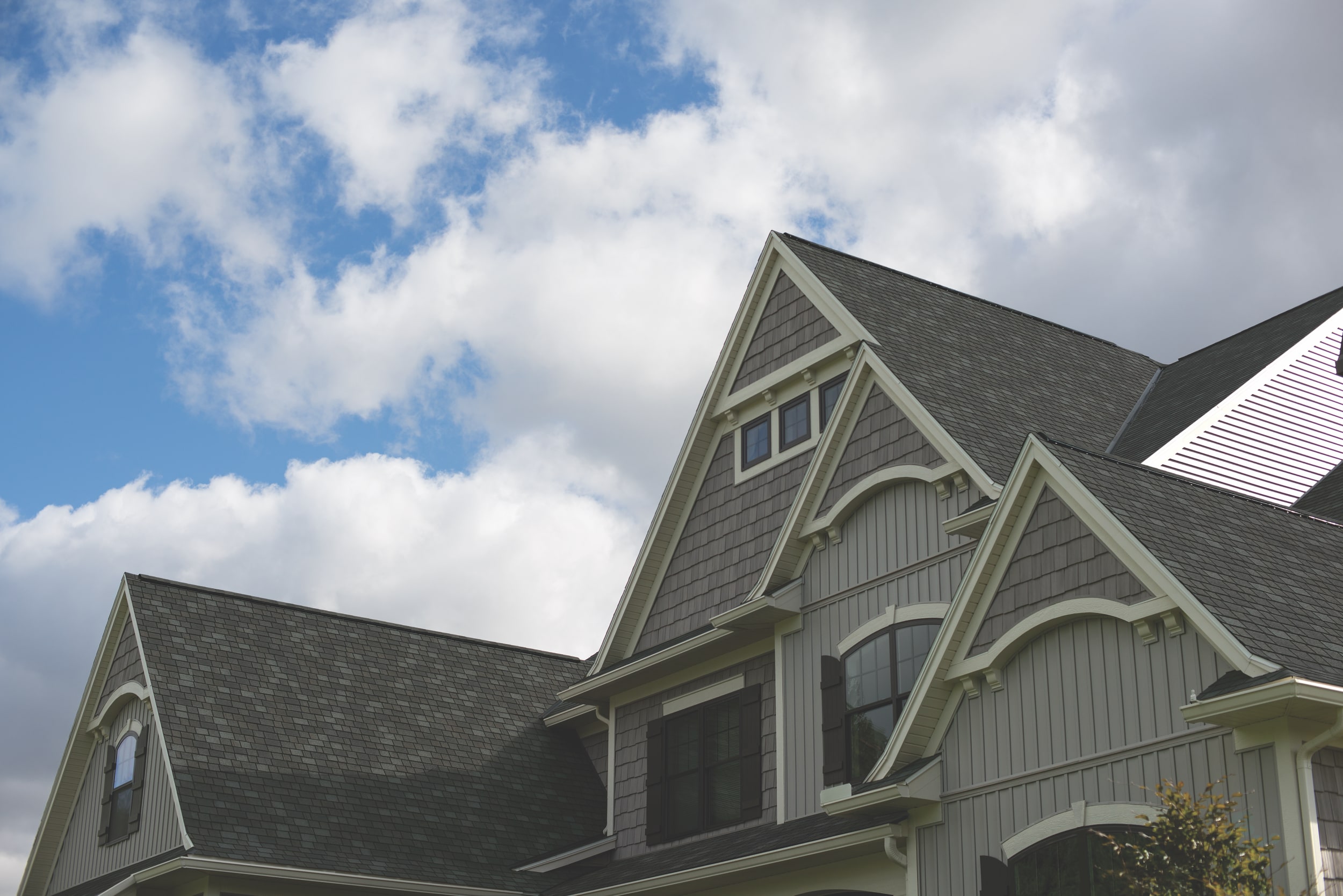 The gabled roof of the two-story house, clad in Mountain Slate shingles, features decorative woodwork and crisp white trim against a partly cloudy sky.
