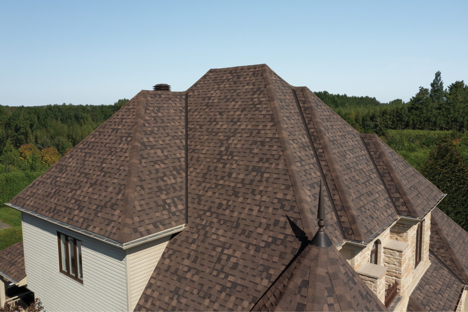 A Shadow Brown shingle roof covers a Nordic-style multi-story house surrounded by trees under a clear blue sky.