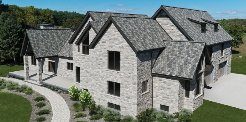 Nordic-style stone house with multiple gabled roofs, surrounded by lush grass and a curved pathway. The exterior showcases gray brickwork and several windows beneath a clear blue sky.
